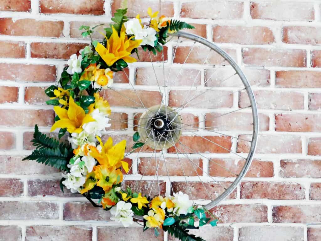 Bicycle Wheel Wreath rim with yellow flowers on brick wall