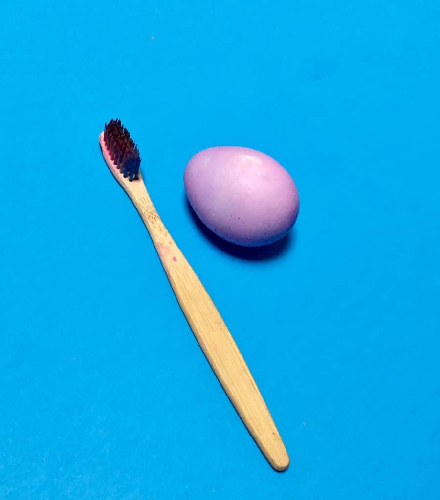 purple dyed egg on blue background next to toothbrush