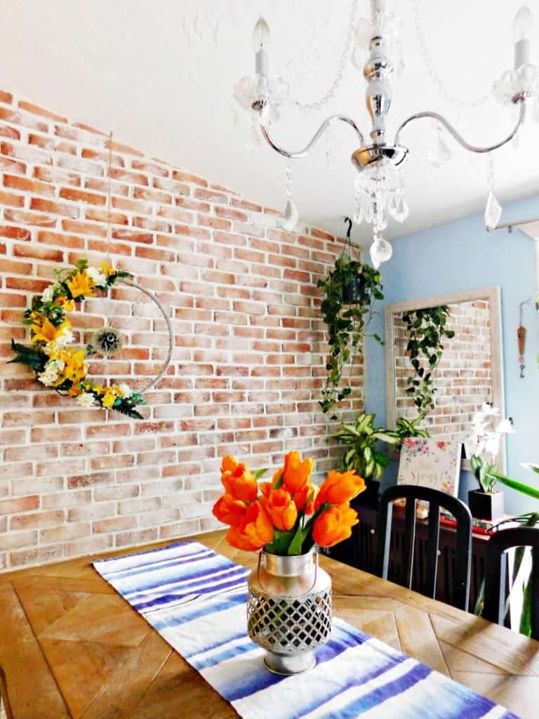 dining room with house plants. Brick wall with wreath and table with orange tulips