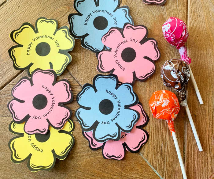 cut out flowers with lollipops laying beside them on a table