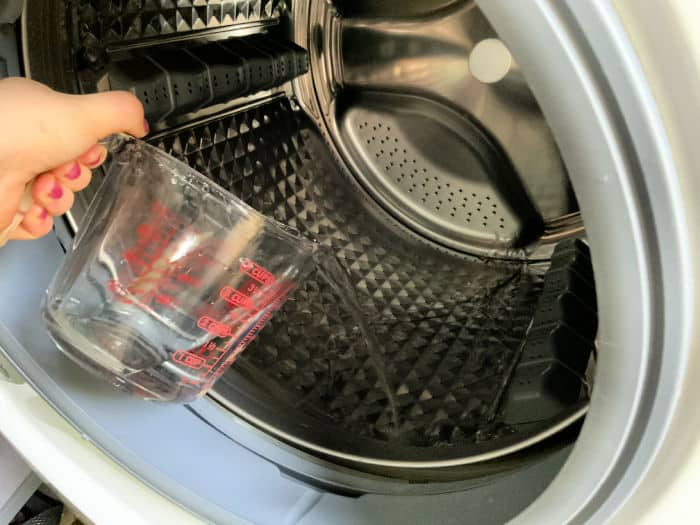 Vinegar being poured into the drum of a front loading washing machine.