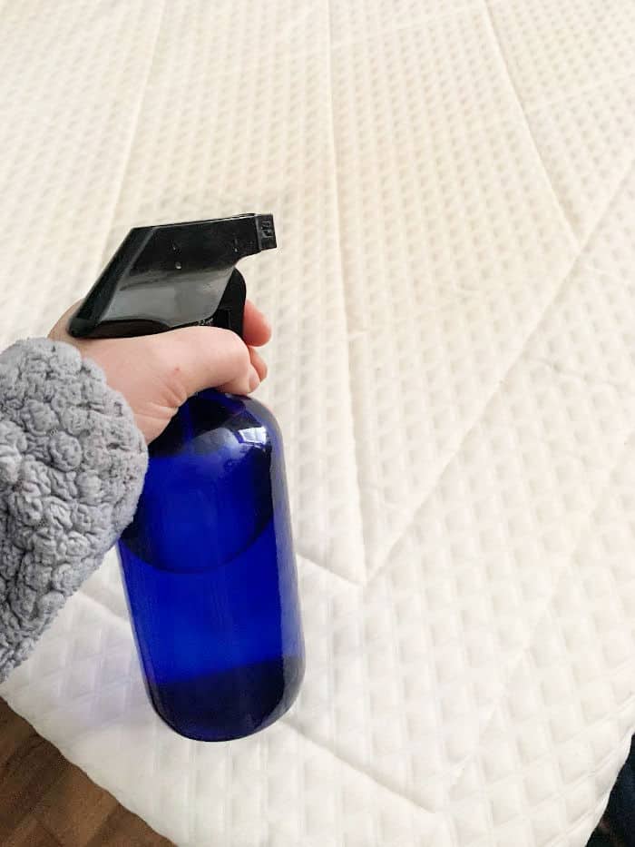 Blue spray bottle spraying mattress with solution. 