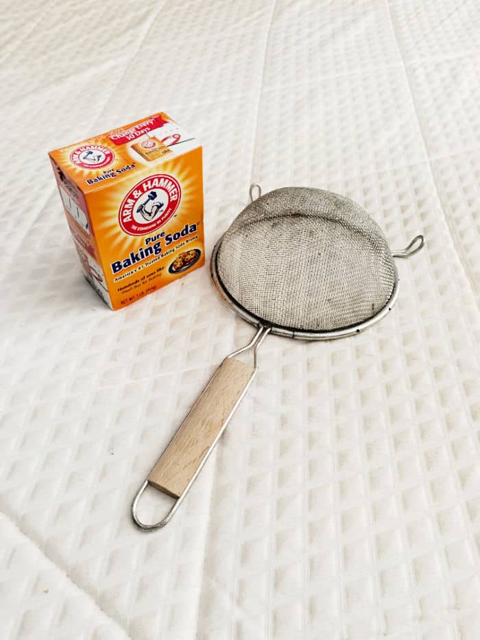 Baking soda and a sifter on a mattress. 