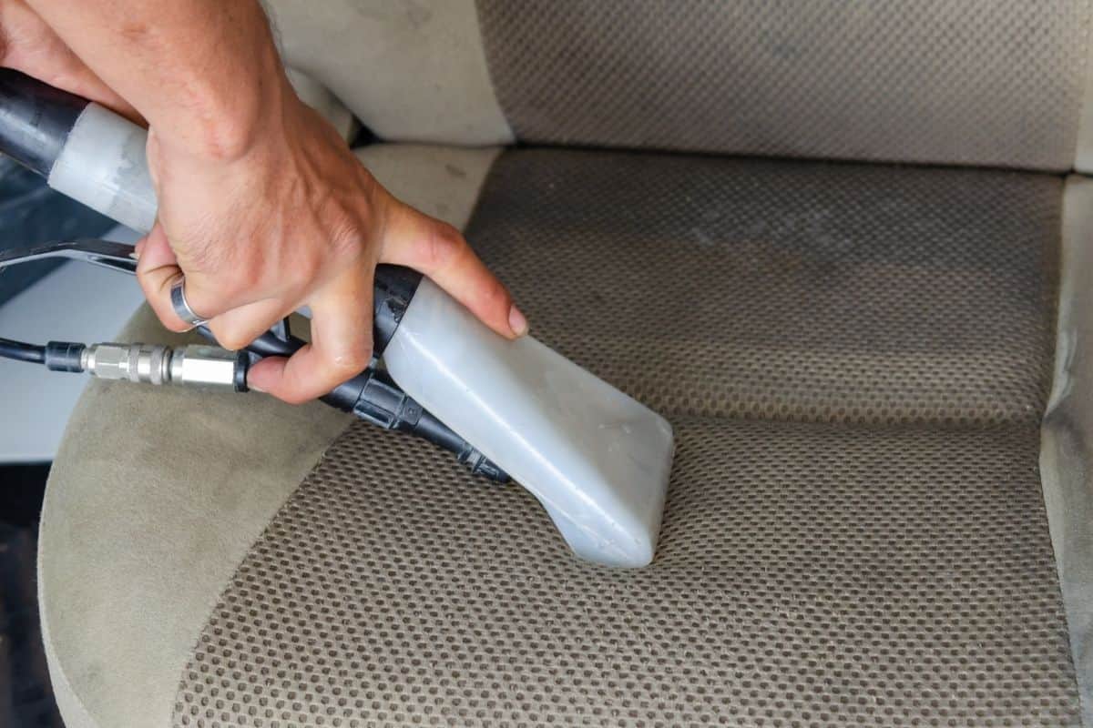 Close up of a hand cleaning a car seat with a vacuum. 