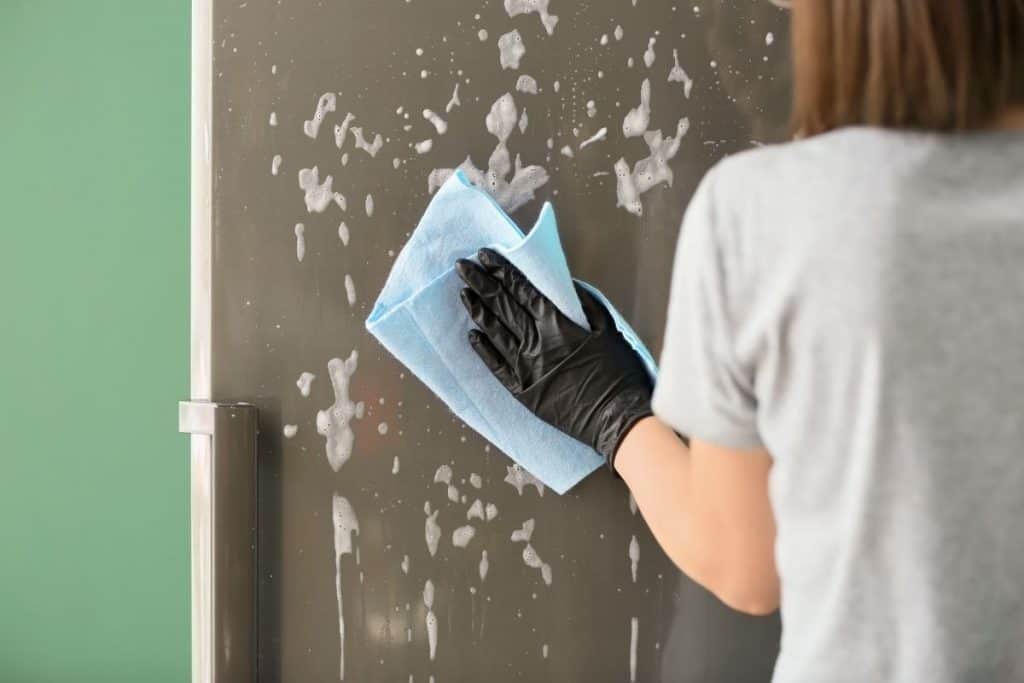 Woman wearing a black glove cleaning a shower door with a blue towel.
