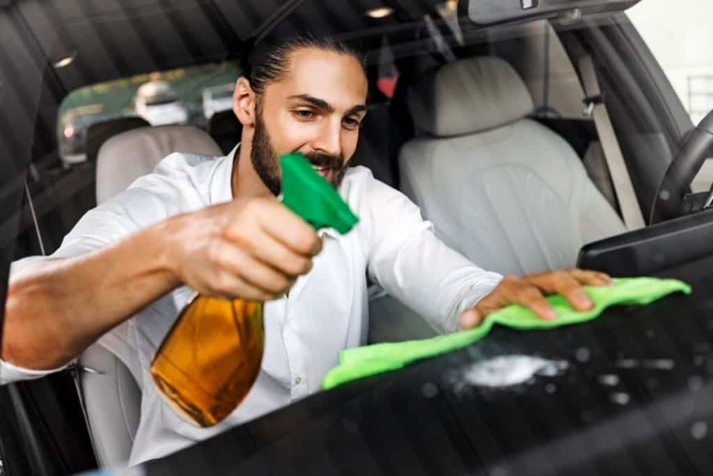 Man cleaning a dashboard with a green microfiber cloth. 