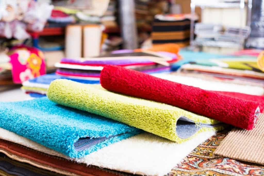 Close up of pieces of red, green and blue wool rugs on a table.