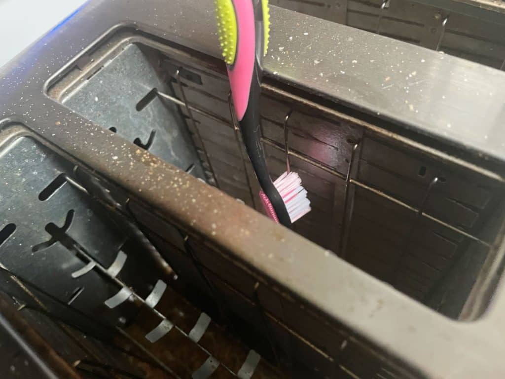 Cleaning a toaster with a clean toothbrush.
