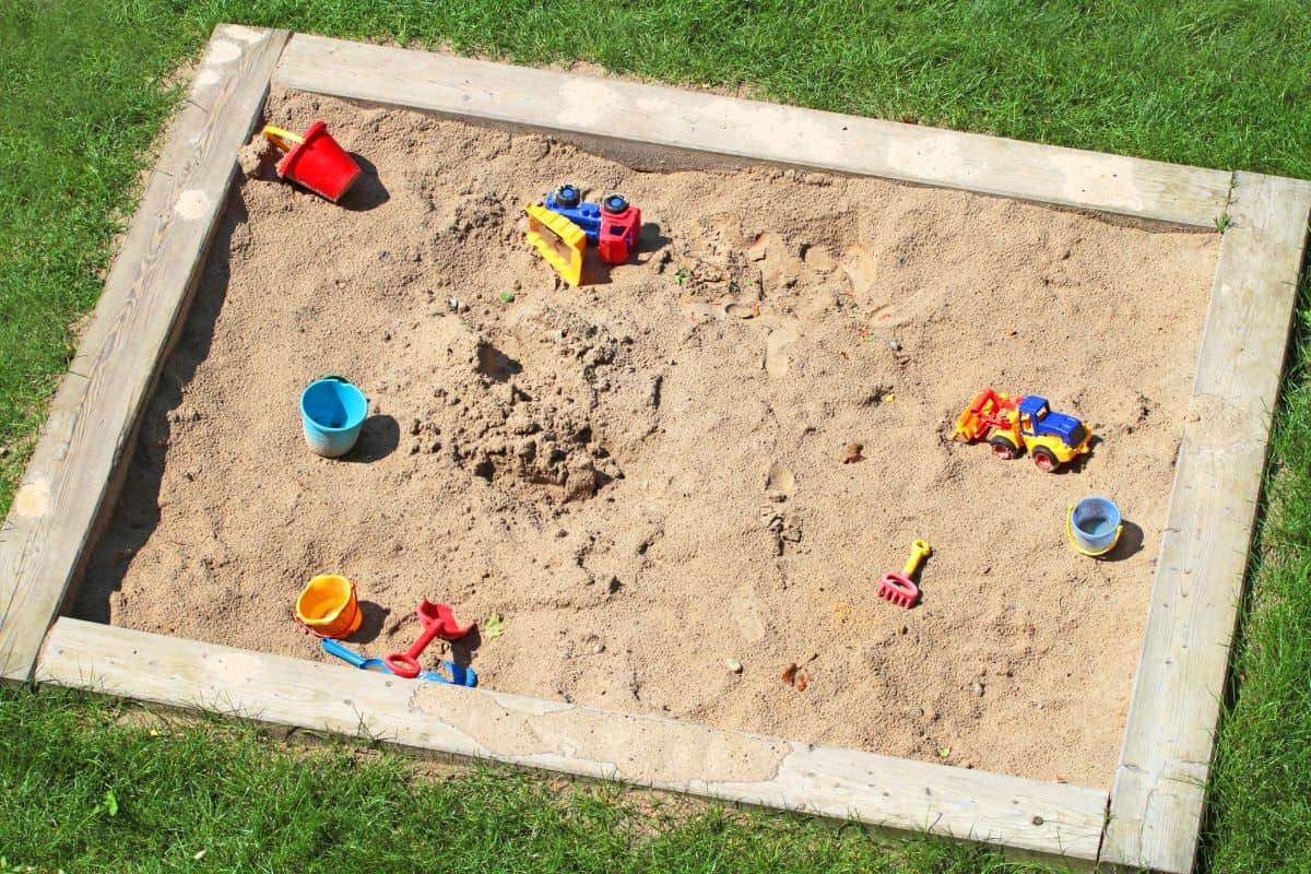 Square sand box filled with sand and toys. 