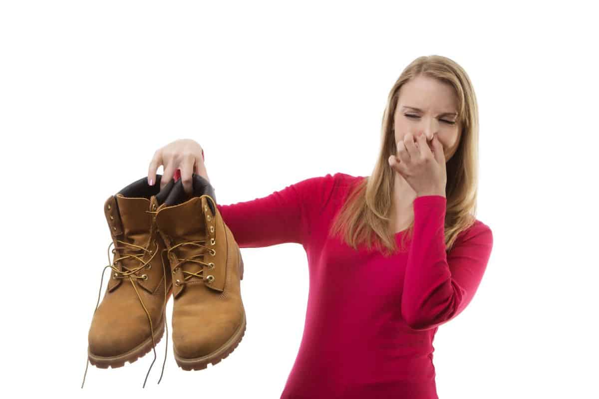 Woman holding a pair of boots while pinching her nose. 