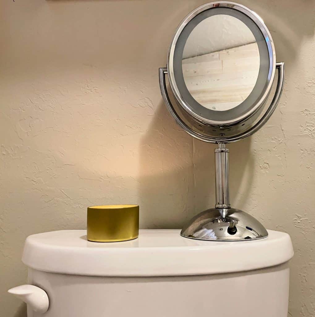 Lit candle on top of the toilet tank next to a small mirror.
