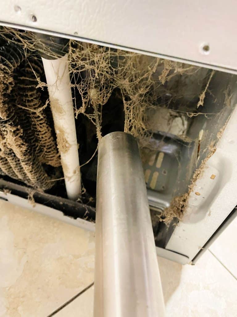 Vacuuming dust from dirty fridge coils.