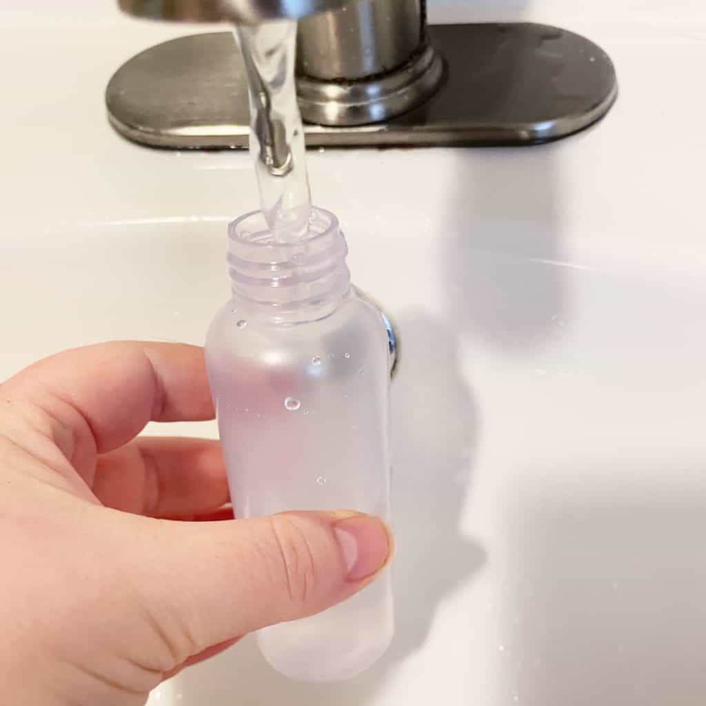 A hand holding a small plastic bottle with water from a bathroom faucet. 