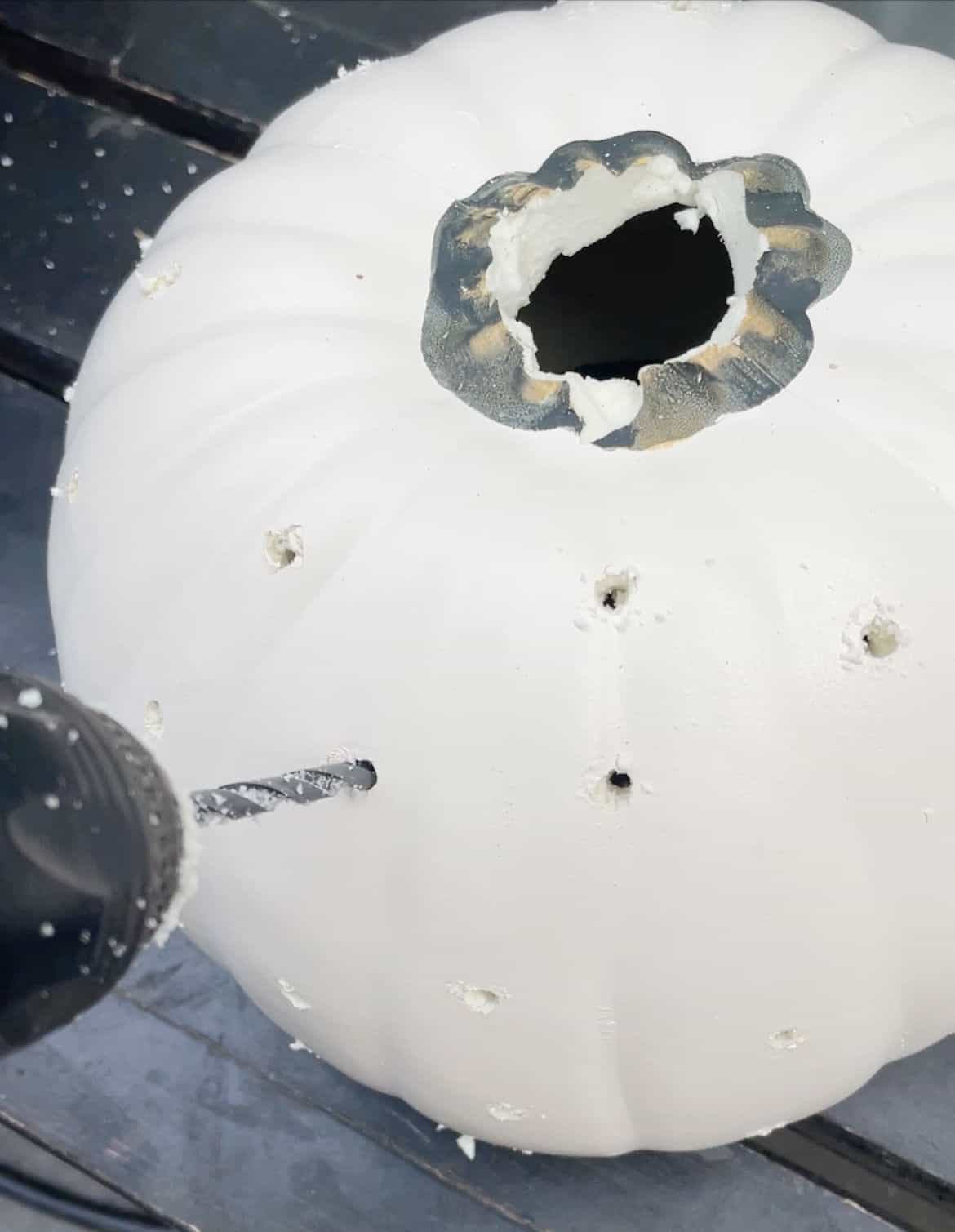 Drilling holes in a white craft pumpkin.