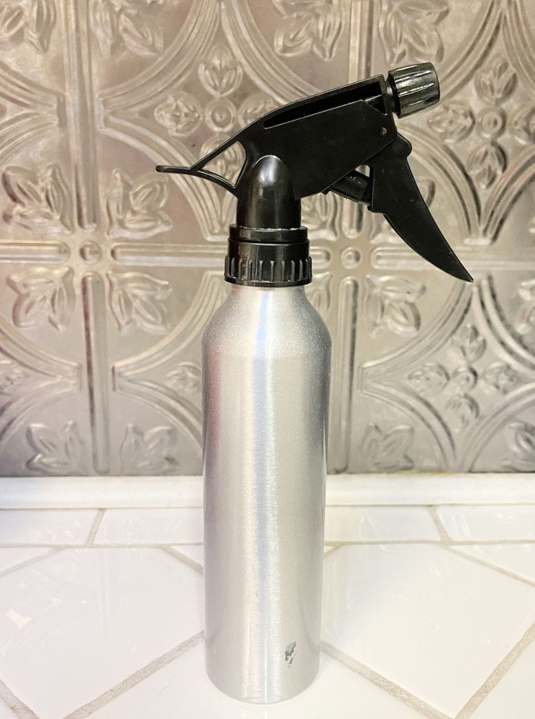Aluminum spray bottle filled with stinging nettle tonic on a counter. 