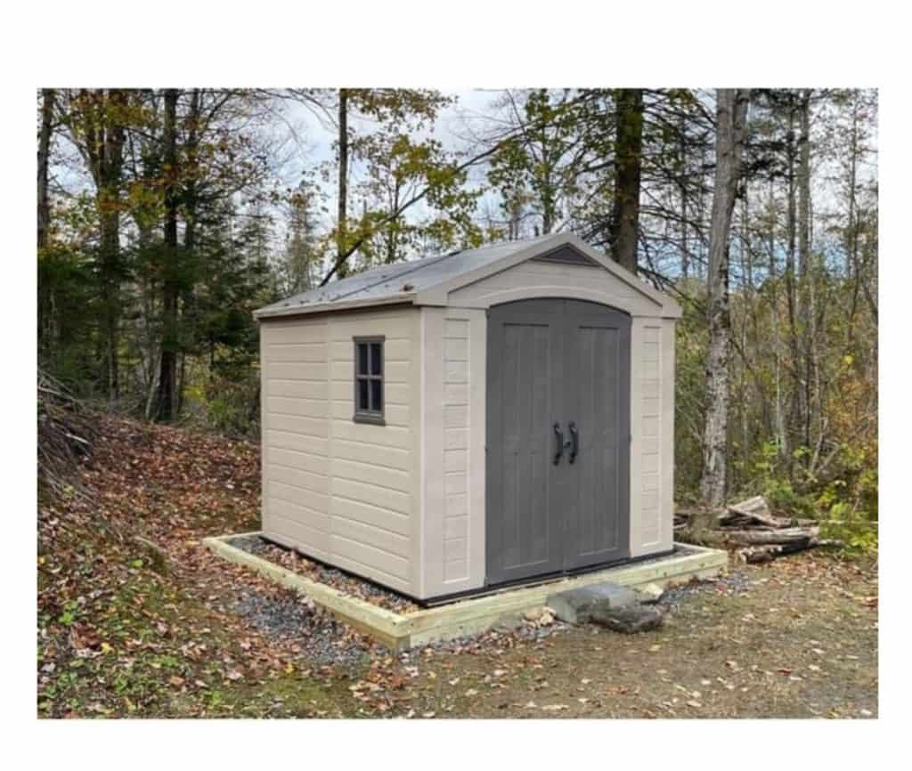 Light grey resin shed placed in a wooded area. 