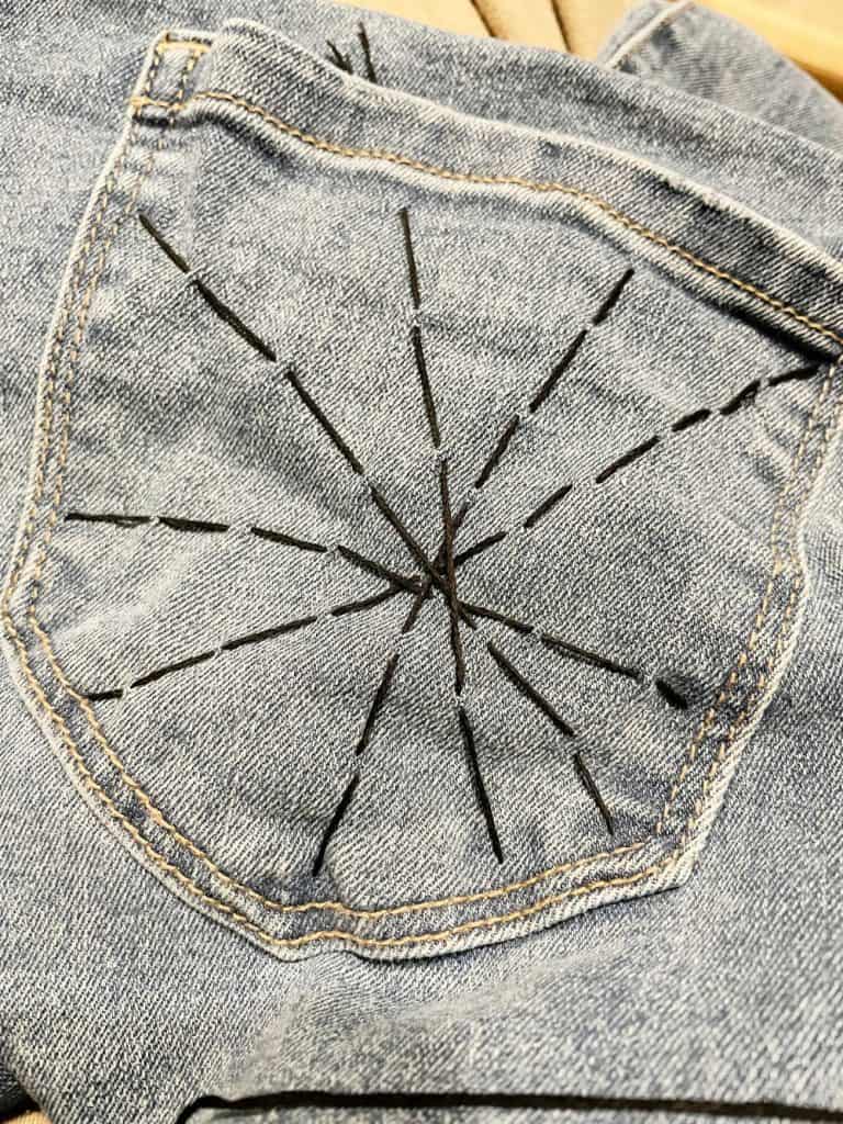 Spider web embroidery on denim pocket, creative fashion accessory, handmade stitched denim design, trendy embroidered jeans detail, relevant for DIY fashion projects