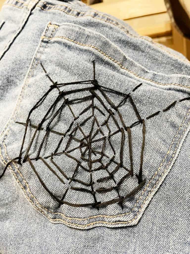 Hand-stitched spider web embroidery on denim pocket, creative craft project for Halloween or spooky themed decor.