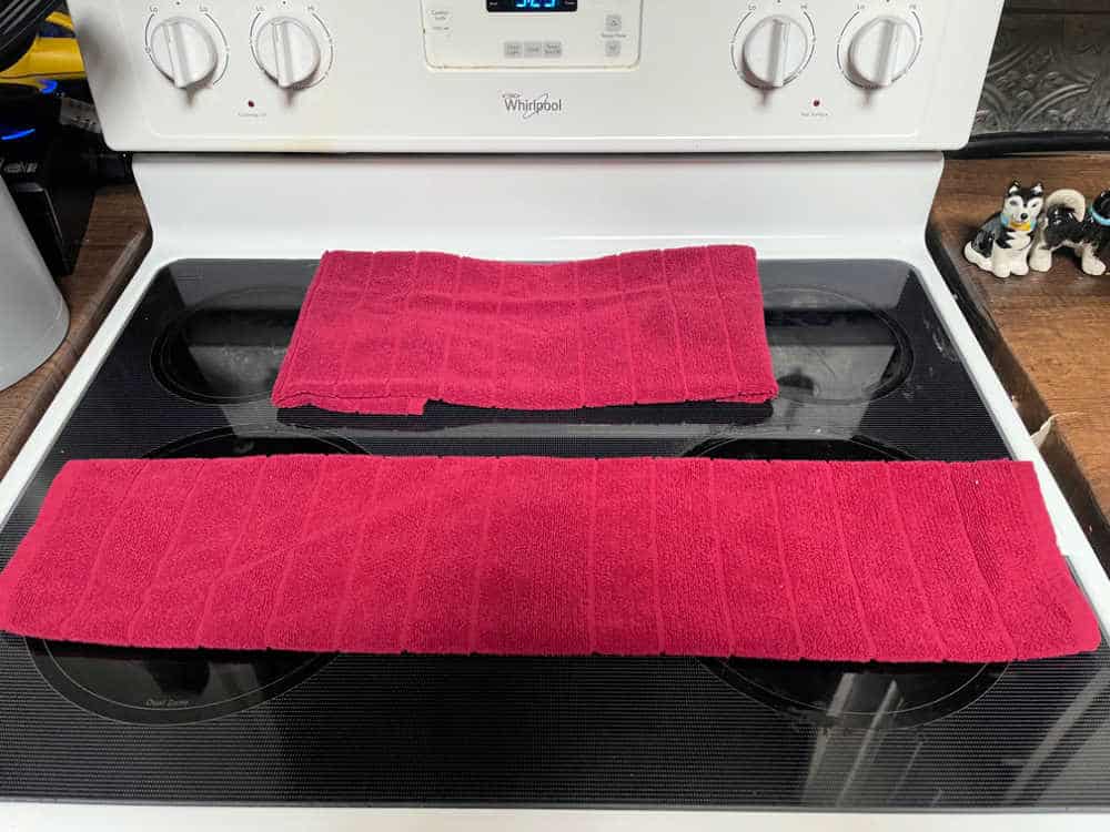 Two red tea towels folded on top of a glass oven. 