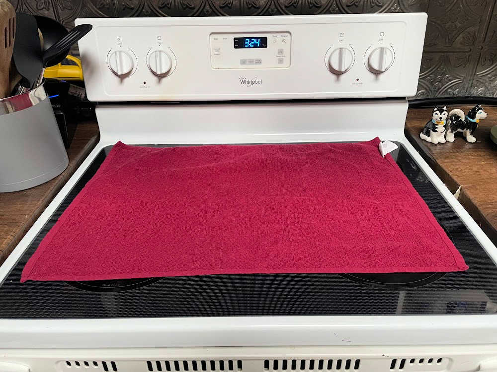 Red tea towel laid flat on the surface of a glass oven top. 